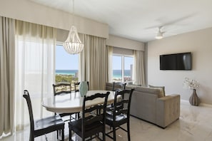 A modern living room with a dining area, a flat-screen TV, and a view of the ocean.