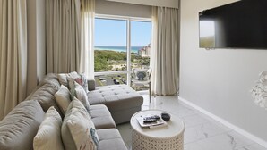 Ein modernes Hotelzimmer mit großem Fenster, einer Couch, einem runden Couchtisch und einem Flachbildfernseher.