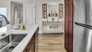 Una cocina moderna con un lavamanos de acero inoxidable, armarios de madera, encimera blanca y elementos decorativos, incluyendo un cuadro de un velero y decoración mural.