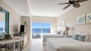 A hotel room with a large bed, a desk with a chair, a television, and a view of the ocean.