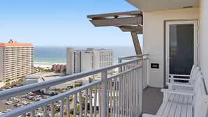 Un balcon donnant sur la plage et l’océan, avec des balustrades blanches et une porte munie d’une moustiquaire.