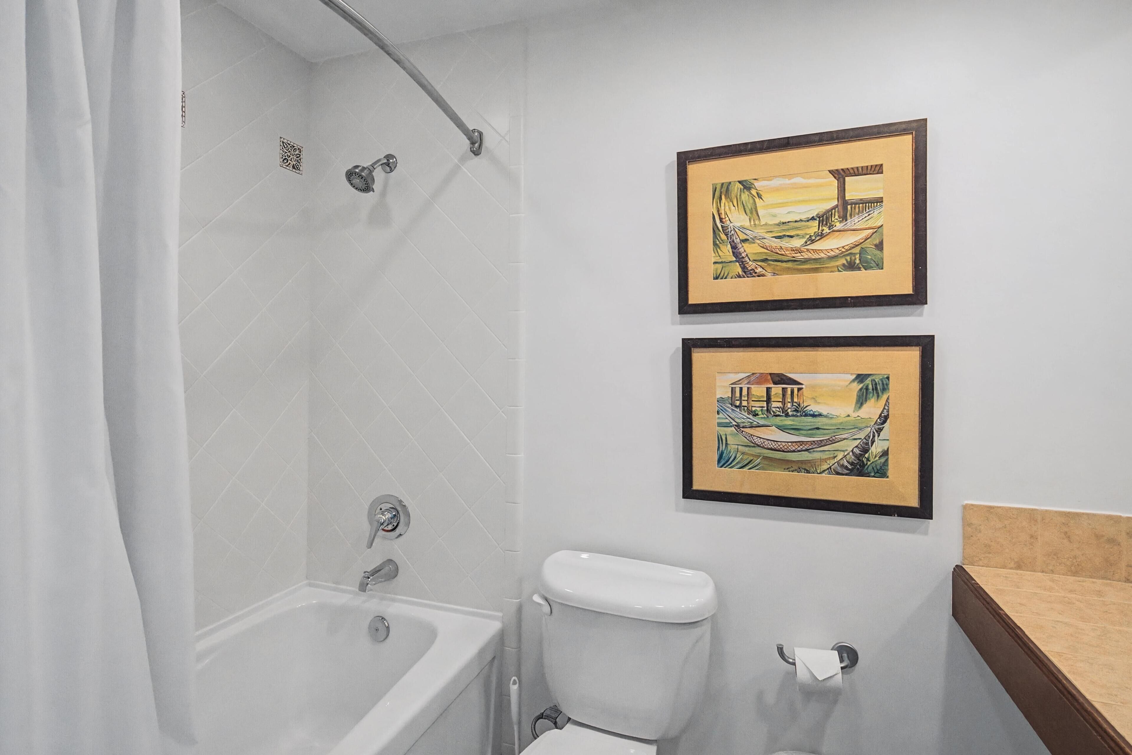 A bathroom with a bathtub, toilet, and two framed pictures on the wall.