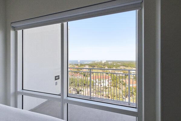 Una habitación con un amplio ventanal que da a un balcón con vistas a una zona residencial y un paisaje distante.