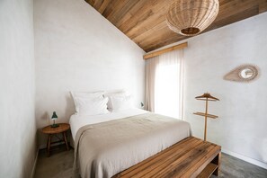 A minimalist bedroom with a wooden headboard, a bedside table with a lamp, a bench, and a wall-mounted mirror. - Quinta do Ameal (Ponte de Lima)