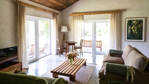 A spacious living room with a wooden ceiling, a television, a coffee table with a vase of flowers, a sofa, and a couch. There are two windows with curtains, a table with chairs, and a painting on the wall. - Quinta do Ameal (Ponte de Lima)