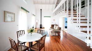 A spacious living area with a wooden floor, a round dining table with chairs, a sofa, and a staircase with white railings. - Quinta do Ameal (Ponte de Lima)