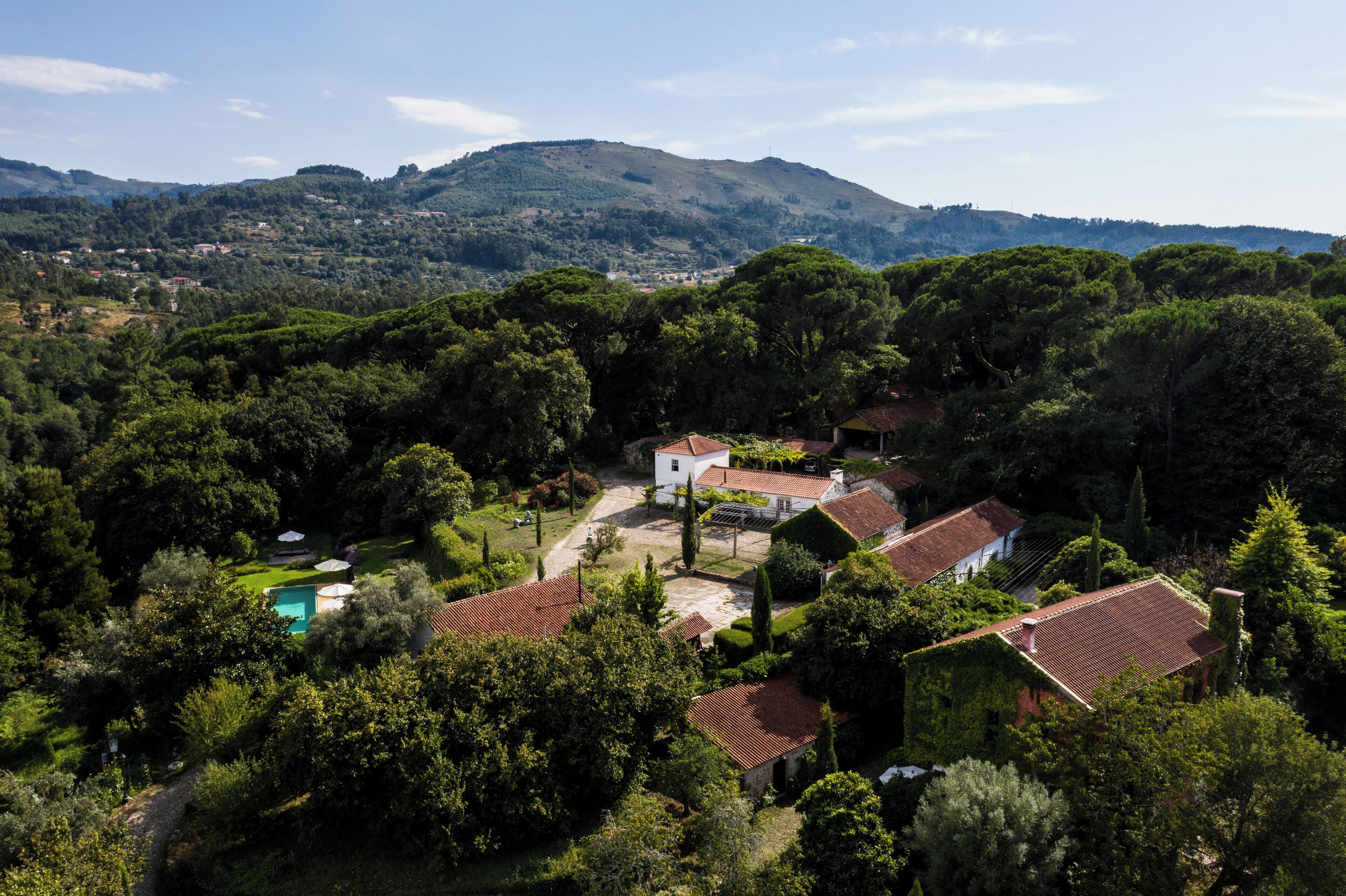 A villa with a swimming pool, surrounded by lush greenery and hills in the background.