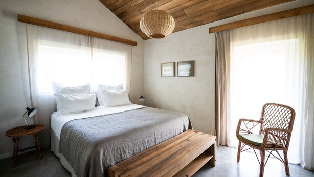 A bedroom with a wooden ceiling, a bed with white linens, a wicker chair, and a woven light fixture. - Quinta do Ameal (Ponte de Lima)