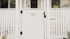 Een wit huis met het nummer 121 op de voordeur, een overdekte veranda en een witte picket-heg.