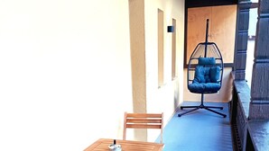 A corridor with a blue floor, wooden chairs and tables, a hanging chair, and a wooden door.