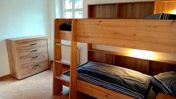 Ein Stockbett mit Holzrahmen, eine Kommode mit Schubladen und ein Fenster mit Blick auf Bäume.