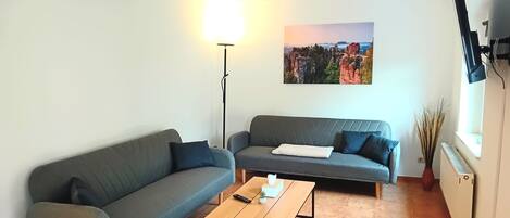 A living room with two grey sofas, a wooden coffee table, a floor lamp, a painting on the wall, and a TV mounted on the wall.