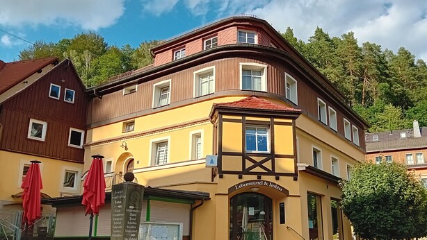 A multi-story building with a yellow facade, a brown upper section, and a red roof.