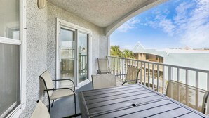 Un balcone con tavolo e sedie, una porta scorrevole in vetro e vista su edifici e alberi.