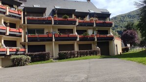 Un hotel de varios pisos con balcones, un estacionamiento y montañas al fondo.