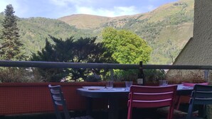 Zona de comedor al aire libre con mesa y sillas, con vistas a un paisaje montañoso.
