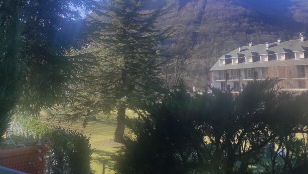 Un edificio con un tejado simétrico y varias ventanas, rodeado de árboles y una montaña al fondo.