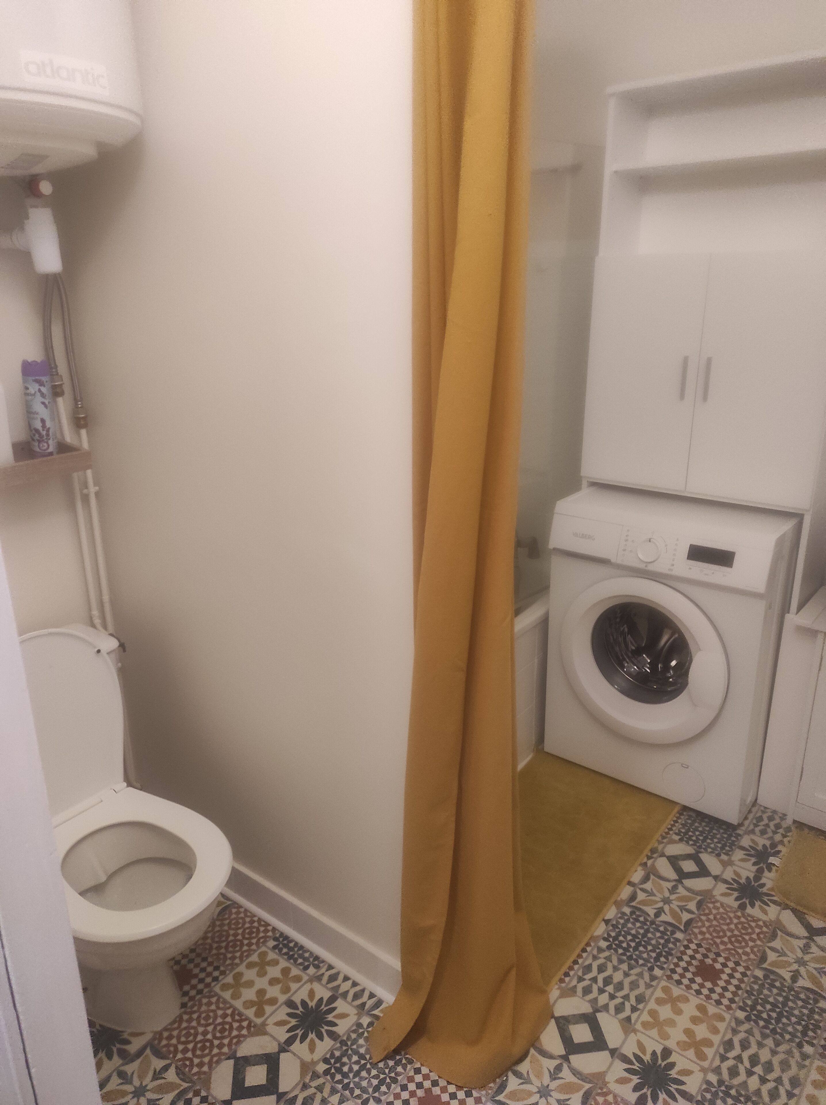 Une salle de bain avec des toilettes, un lave-linge et un rideau de douche jaune.