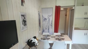 Un comedor con una mesa dispuesta para cuatro personas, sillas blancas, un televisor y una figurita de vaca.