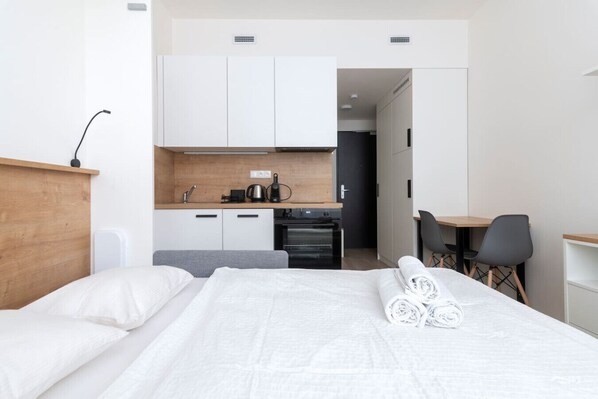 A hotel room with a bed, a desk, a chair, a kitchenette, and a bathroom.