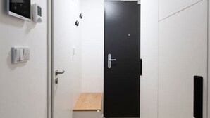 Un couloir étroit, avec une porte au fond, un petit banc en bois et un panneau de commande fixé au mur.