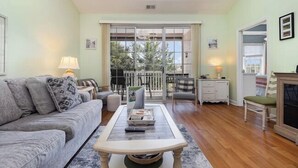 Un salon avec un canapé, une table basse et une cheminée. Il y a un balcon avec vue sur les arbres.