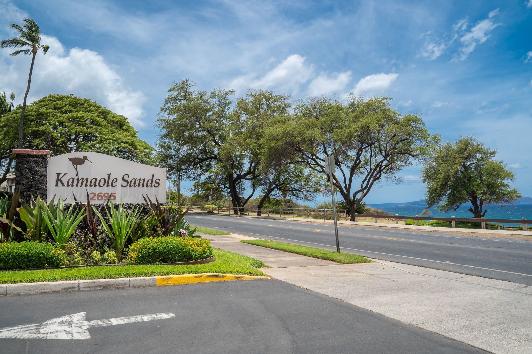 A road sign for Kamaole Sands with a scenic view of trees and a clear sky.