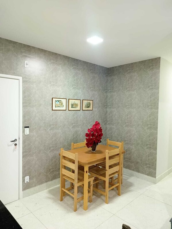 A dining area with a wooden table and chairs, a vase with red flowers, and three framed pictures on the wall.