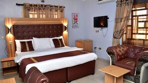 A bedroom with a large bed, a leather sofa, a bedside table, a TV, and a window with curtains. - Prenox Hotel and Suites  (Benin City)