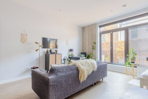 A modern living room with a sofa, a flat-screen TV, a floor lamp, and a large window. - Stylish Studio in Hackney with Private Terrace (Greater London)