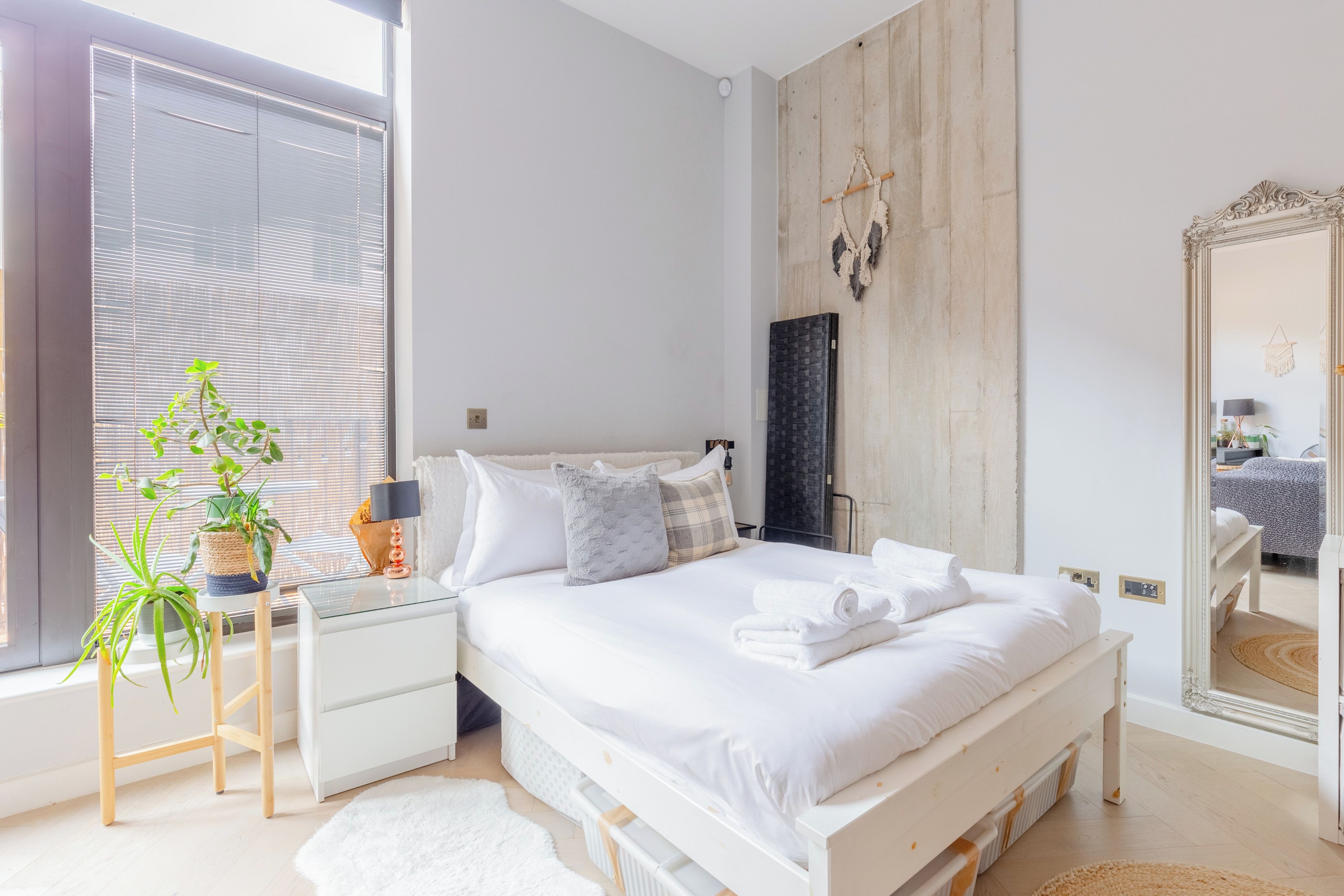A modern bedroom with a large bed, bedside tables, a mirror, and a window with blinds.
