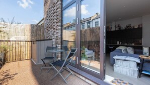 A modern outdoor patio with a glass door leading to a living area, a wooden fence, and a small table with chairs. - Stylish Studio in Hackney with Private Terrace (Greater London)