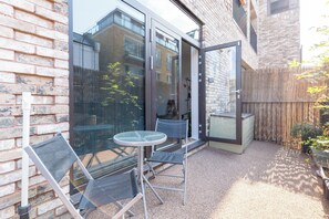 Eine Terrasse mit einem Glastisch und Stühlen, einer Ziegelwand und einem Holenzaun.