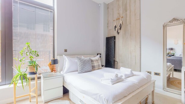 A bedroom with a bed, bedside tables, a mirror, and a window with blinds. - Stylish Studio in Hackney with Private Terrace (Greater London)
