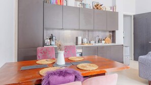 A modern kitchen with grey cabinets, a wooden dining table with woven placemats, and a vase with dried flowers. - Stylish Studio in Hackney with Private Terrace (Greater London)