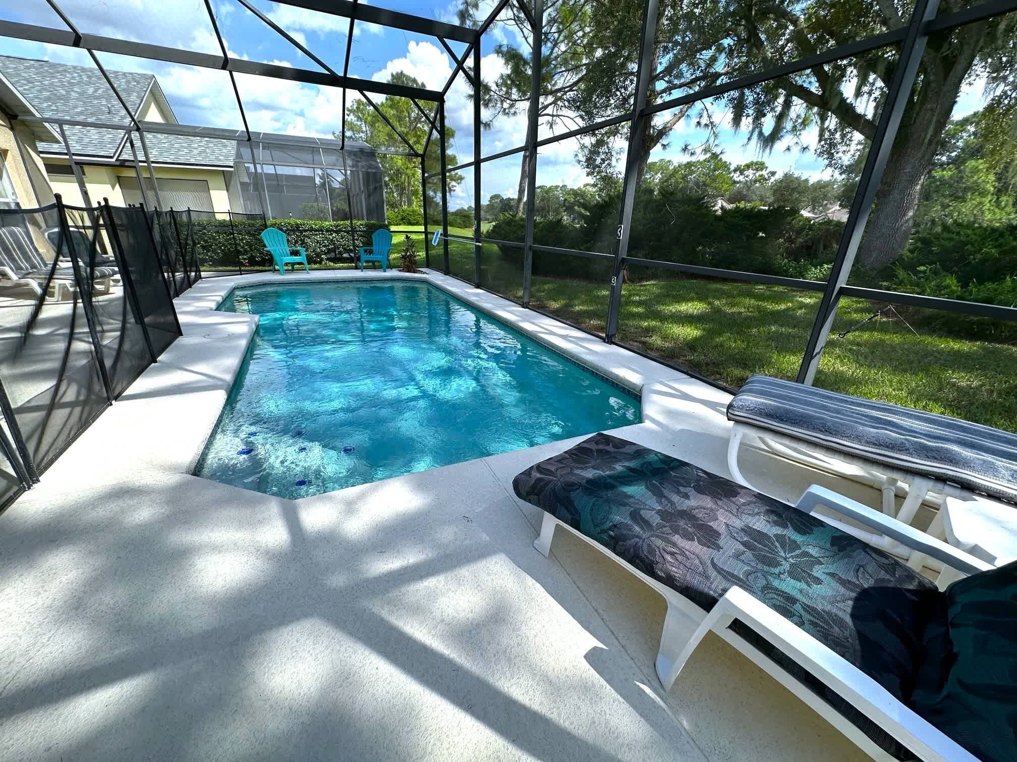 Una piscina con una banca sumergida y sillas, rodeada por una estructura de vidrio.