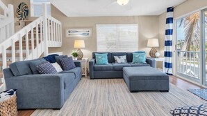 A modern living room with a grey sectional sofa, a white staircase, and a ceiling fan. - AMI's Salty Breeze: 5-min walk to Beach, community pool, relaxing decor (Holmes Beach)
