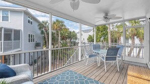 A covered outdoor deck with a railing, two ceiling fans, and a seating area with chairs and a sofa. - AMI's Salty Breeze: 5-min walk to Beach, community pool, relaxing decor (Holmes Beach)