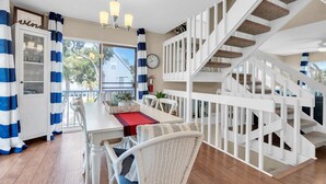 A dining area with a white table, chairs, and a red runner. There is a white staircase with a view of the outside. - AMI's Salty Breeze: 5-min walk to Beach, community pool, relaxing decor (Holmes Beach)