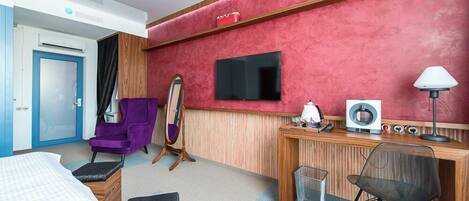 A hotel room with a bed, a desk with a computer, a chair, a TV, and a mirror.