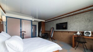 Quarto de hotel com uma cama grande, uma escrivaninha com computador, televisão e espelho.