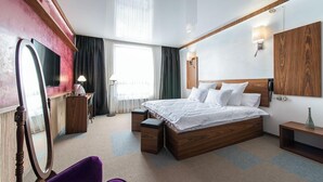 Quarto de hotel moderno com uma cama grande, uma mesinha de toucador com espelho, uma escrivaninha e uma janela com cortinas.