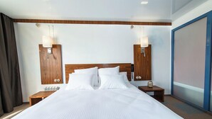 Quarto de hotel com cama grande, cabeceira de madeira, duas mesas de cabeceira com abajures e uma janela ampla com vista.