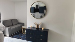 A modern living room with a grey sofa, a round coffee table, a black cabinet with drawers, a round mirror, and a vase with dried plants. - Spacious & comfortable apartment near Paris, fully renovated (2 rooms) (Franconville)