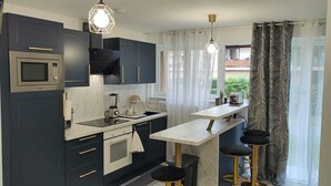 A compact kitchen with dark cabinetry, a built-in oven, a microwave, a sink, and a small dining area with stools. - Spacious & comfortable apartment near Paris, fully renovated (2 rooms) (Franconville)