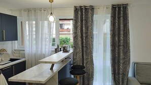 A compact kitchen with a countertop, a hanging light fixture, and a view of the outdoors through sheer curtains. - Spacious & comfortable apartment near Paris, fully renovated (2 rooms) (Franconville)