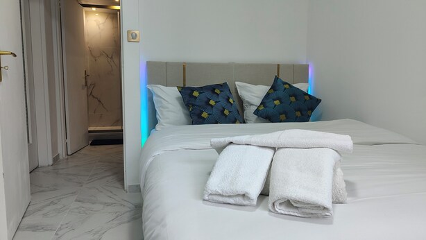 A hotel room with a bed, white linens, two patterned pillows, and a set of towels. - Spacious & comfortable apartment near Paris, fully renovated (2 rooms) (Franconville)