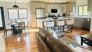 Una cocina amplia con electrodomésticos modernos, un comedor con mesa y sillas redondas, y un gran sofá de cuero en la sala.