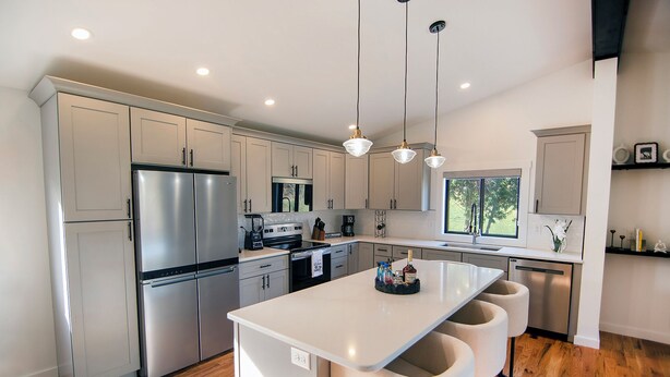 Una cocina moderna con electrodomésticos de acero inoxidable, una isla central con taburetes altos e iluminación colgante.