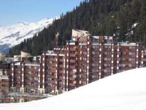 A multi-story hotel with a modern architectural design, located in a mountainous area with snow-covered peaks in the background. - Ski-in/ski-out & foot of the slopes, 5th floor, view ski slopes, balcony, tv, 28m², La Plagne (La Plagne)
